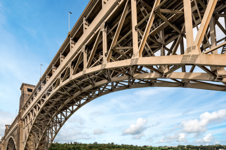 A large metal bridge arching over a river with a blue sky background.