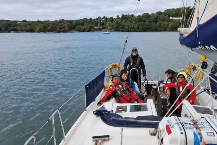 Group of people sailing on a boat in a lake surrounded by trees under a cloudy sky.