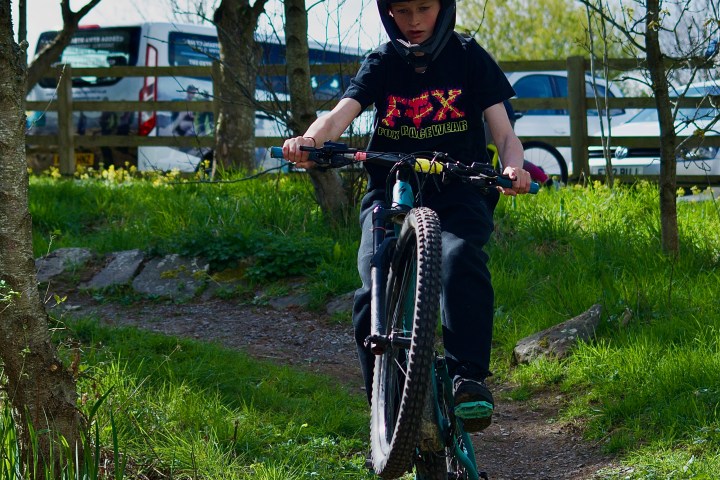 Person in helmet doing a wheelie on a dirt path through trees.
