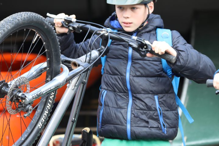 Child wearing a helmet, holding a bicycle upright, dressed in a puffer jacket and green pants.