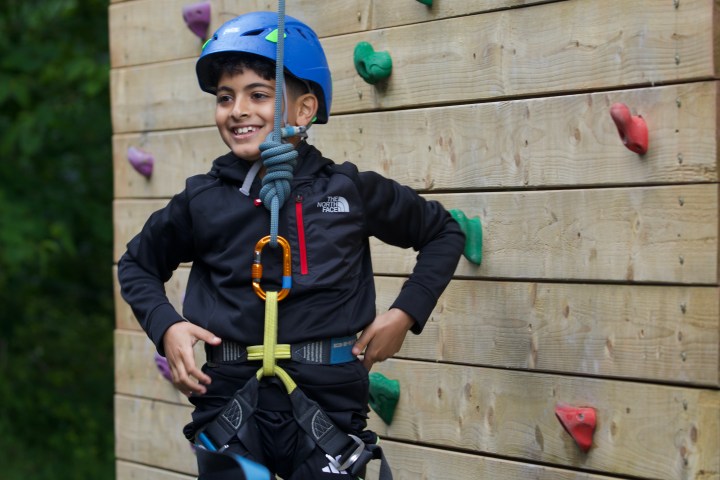 Young boy in helmet climbing a wall with colorful holds.