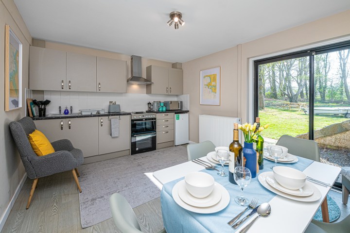 Modern kitchen-dining area with beige cabinets, table set for four, and view of garden through glass door.