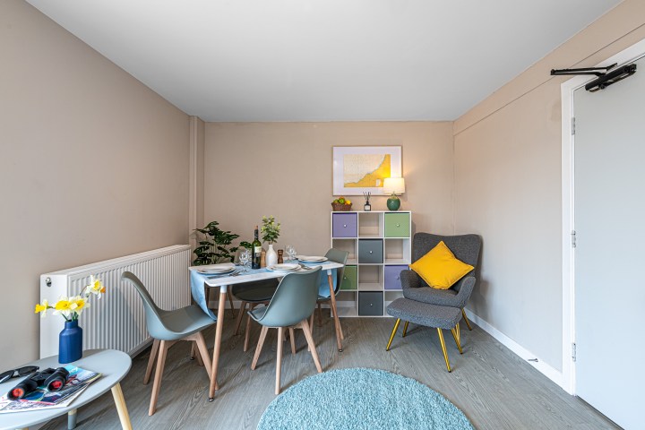 Modern dining room with table, chairs, armchair, colorful shelves, and decor.