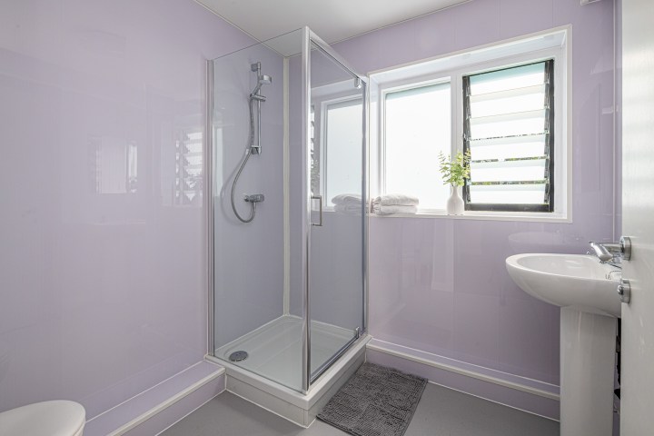 Modern bathroom with shower, purple walls, window, and white sink.