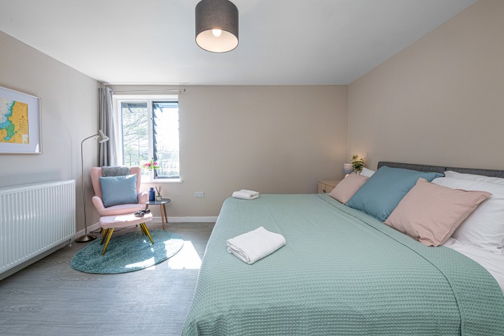 Modern bedroom with teal bedding, pink chair, and window with natural light.