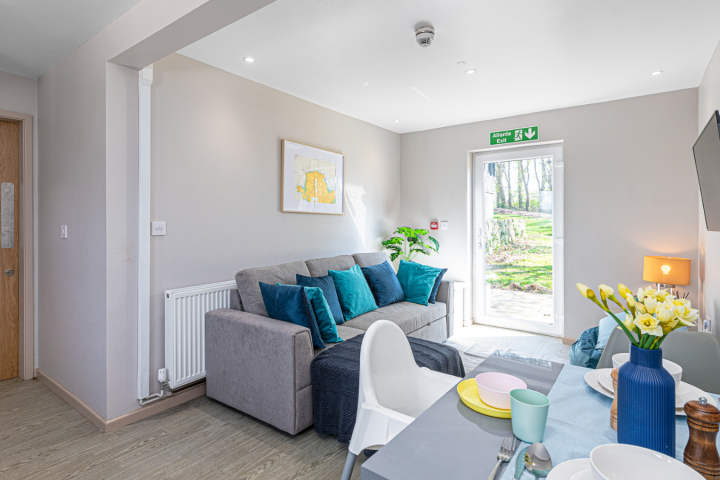 Modern living room with sofa, TV, dining table, and glass door leading to garden.