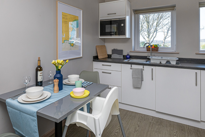 Modern kitchen with dining table set for two, white cabinets, and window view.