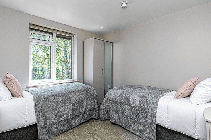 Room with two single beds, gray bedding, window, and a wardrobe.