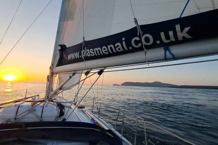 Sailing boat at sunset with distant land and calm sea.