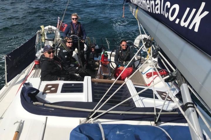 Four people sailing on a boat with visible sails and ocean waves.