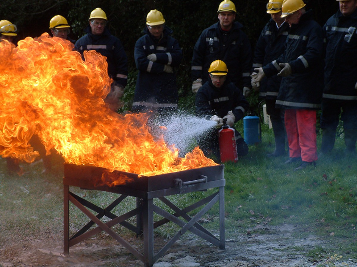 Firefighters extinguishing outdoor fire with extinguisher.