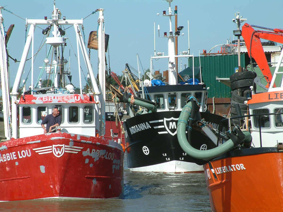 Fishing boats docked with equipment in a harbor.