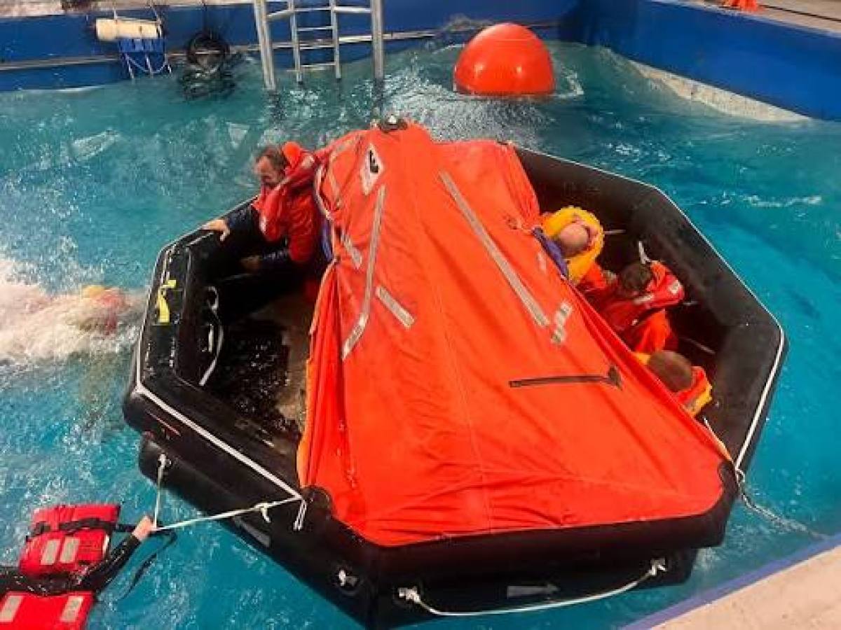 People in water survival training with an orange life raft in a pool.
