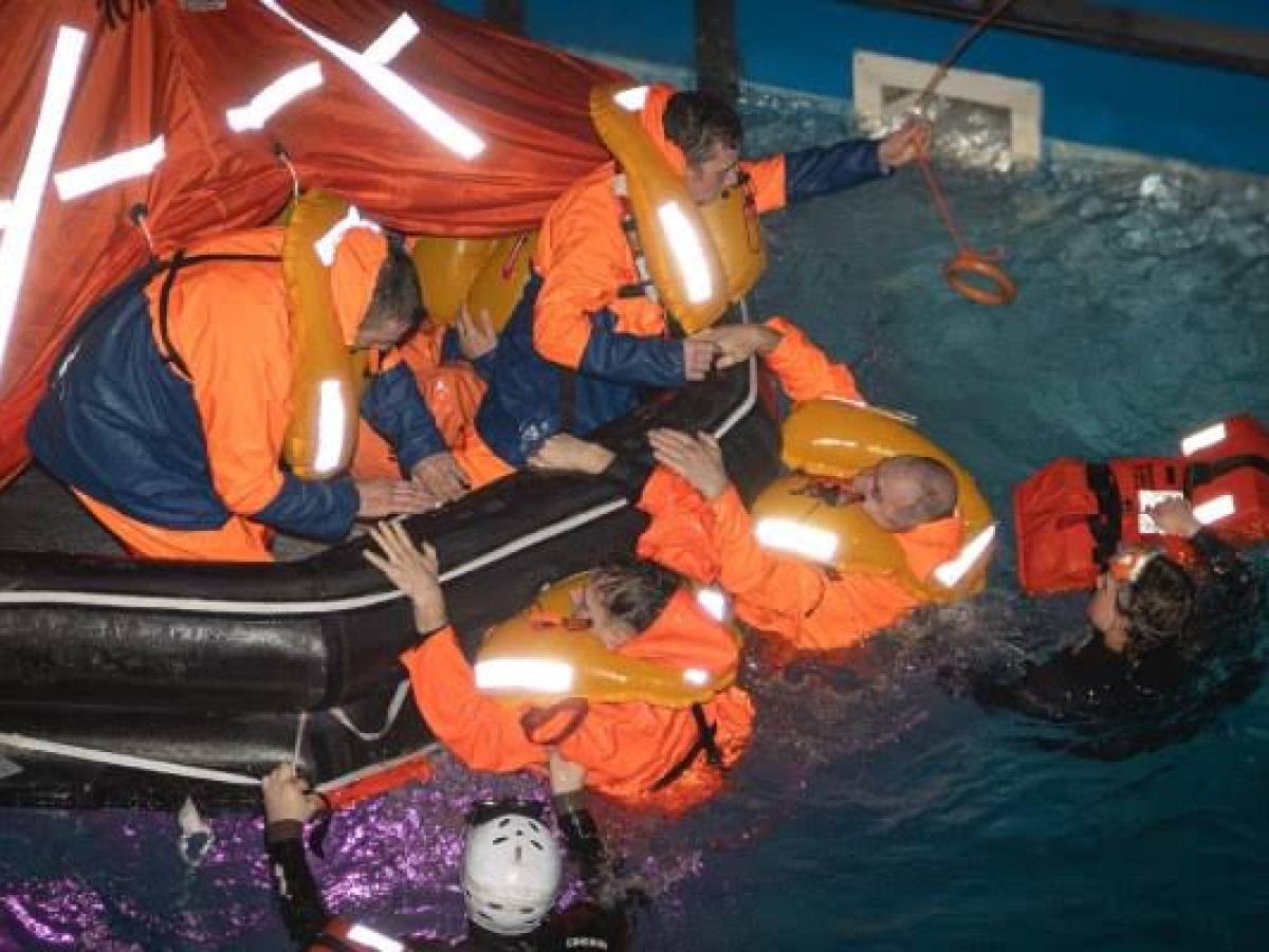 People in life jackets are assisted into a raft in a swimming pool training exercise.