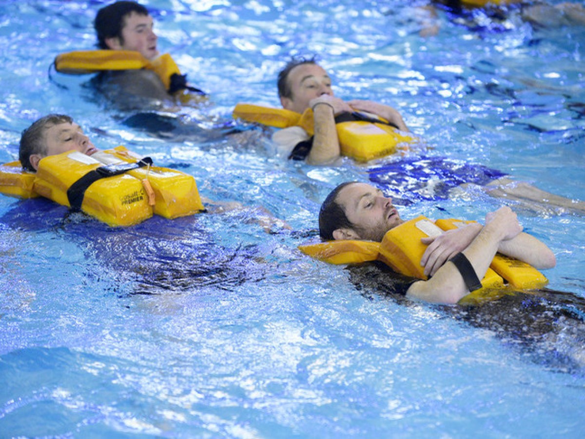 Four people in a pool wearing yellow life vests, floating on their backs.